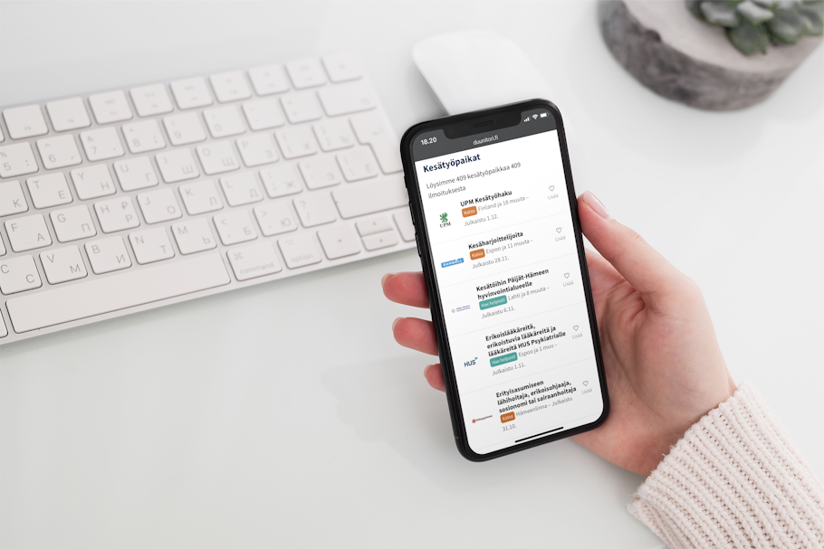 Henkilö pitää kädessä puhelinta, jossa näkyy Duunitorin tämän hetken avoimia kesätyöpaikkoja esimerkiksi UPM:llä ja terveydenhuollossa.